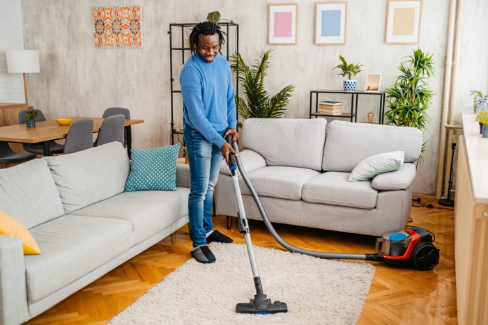 Un beau jeune homme noir passe l'aspirateur sur la moquette de son appartement.