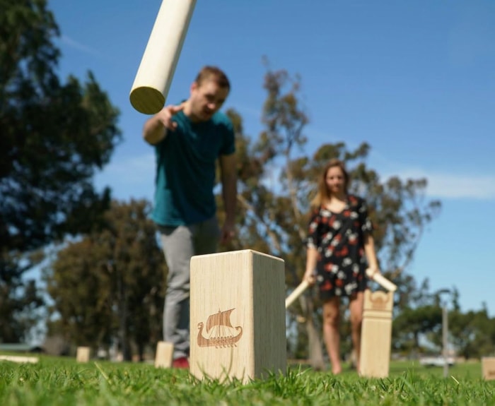 Deux personnes jouent au jeu en bois Kubb dans la cour.