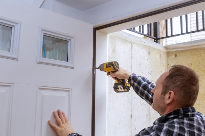 crédit d'impôt pour l'efficacité énergétique - homme avec perceuse - accrochant une porte d'entrée blanche