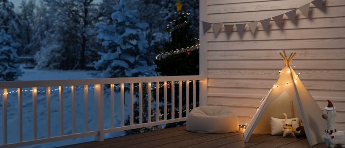 Balustrade et revêtement de porche blancs, lit pour chien et tipi de taille enfant décoré de guirlandes lumineuses blanches sur le porche.