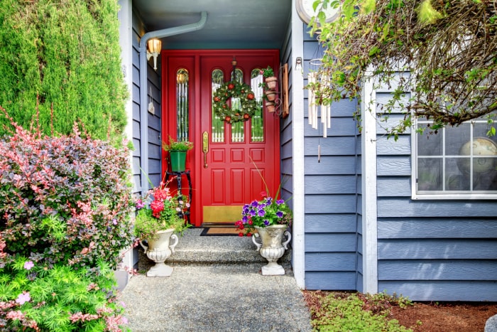 Maison moderne bleue avec porte rouge et allée pavée.