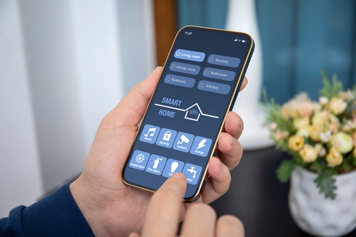 les mains d'un homme tiennent un téléphone avec une application de maison intelligente sur l'écran dans la maison
