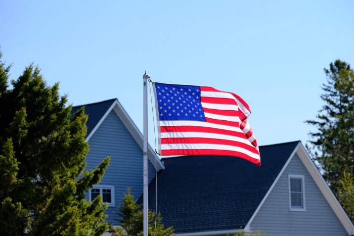 Drapeau américain flottant devant le toit d'une grande maison de banlieue