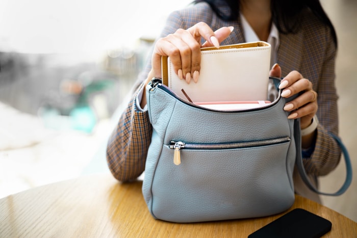 Une femme sort un carnet d'un sac bleu clair posé sur une table.