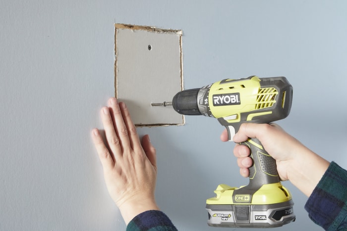 Une femme utilise des vis pour cloisons sèches pour fixer une plaque de plâtre au montant du mur.