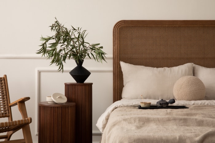 Une chambre à coucher avec un cadre de lit en bois et une chaise à bascule, une couette en lin et une plante sur la table de nuit.