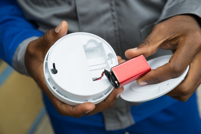 Gros plan des mains d'un électricien retirant la batterie du détecteur de fumée