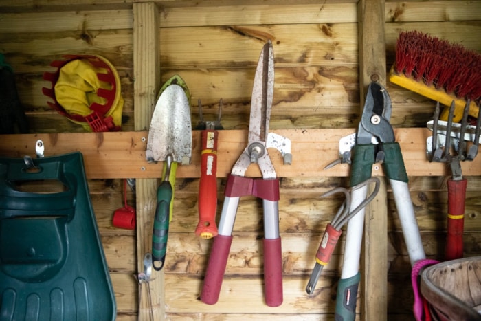 Une truelle, un sécateur et d'autres outils de jardinage accrochés au mur d'un hangar.