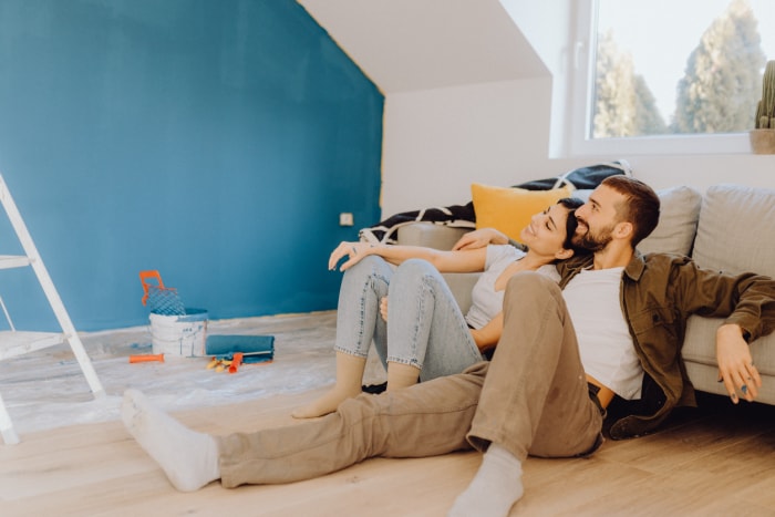 Un jeune couple est assis par terre et admire un mur turquoise fraîchement peint qu'ils ont peint ensemble.