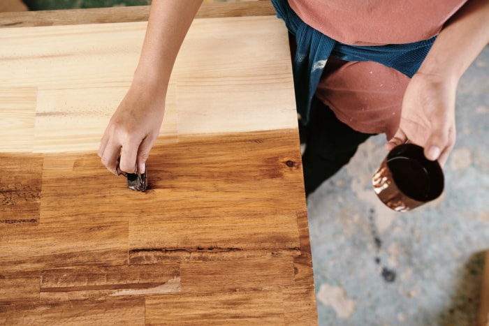 Les mains d'un menuisier appliquent un vernis à bois sur une planche de boucherie en bois à l'aide d'une éponge. 