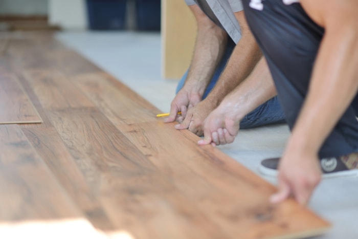 Deux hommes sont à genoux sur le sol pendant qu'ils installent un parquet stratifié en bois.