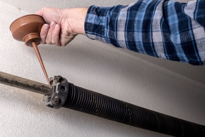 Gros plan d'un composant de porte de garage et d'une personne en chemise à carreaux utilisant un outil pour le réparer. 