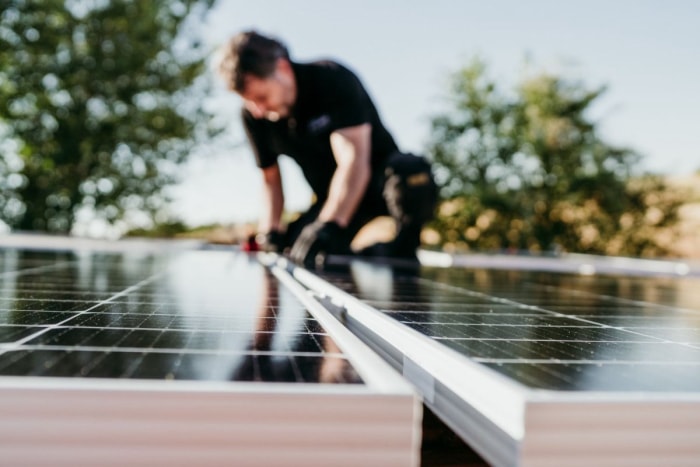 Un ouvrier vêtu de noir installe des panneaux solaires sur un toit.