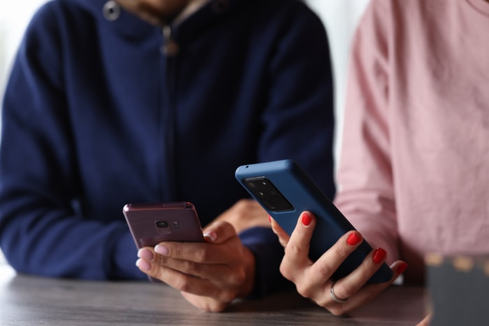 Deux femmes tenant à proximité l'une de l'autre des smartphones de marques différentes.