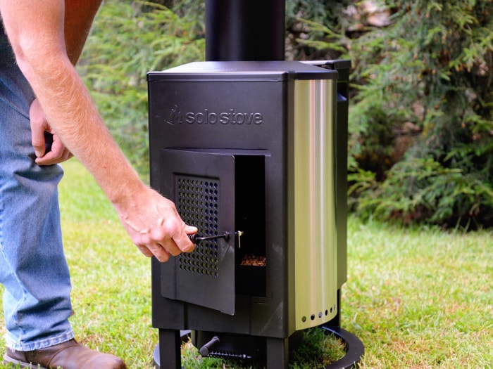 Personne ouvrant la porte du foyer d'un chauffage de terrasse à tour Solo Stove.