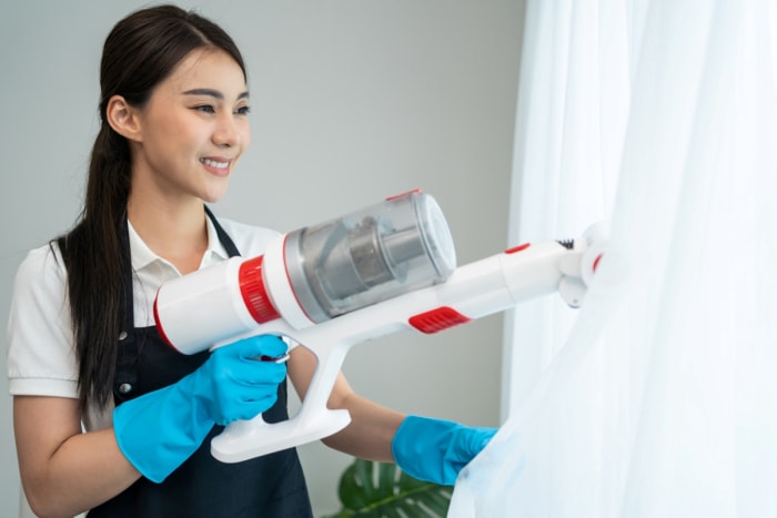 Femme utilisant un aspirateur sur des rideaux