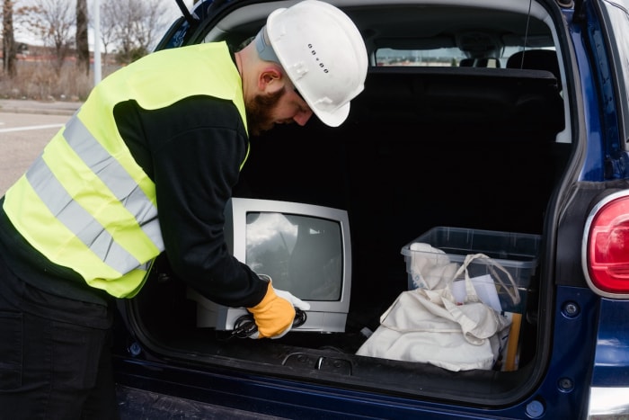 Un éboueur décharge un vieux téléviseur d'un coffre pour le recyclage des déchets électroniques.