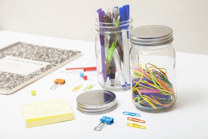 Bocaux en verre transparent contenant des fournitures de bureau colorées sur un bureau blanc