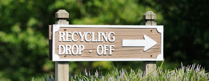 Panneau en bois avec une flèche indiquant « point de collecte du recyclage ».