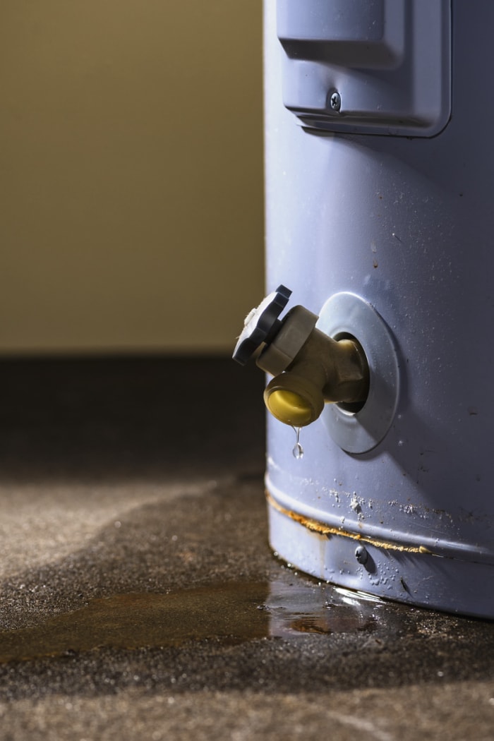 Fuite d'eau du robinet en plastique d'un chauffe-eau électrique résidentiel posé sur un sol en béton.