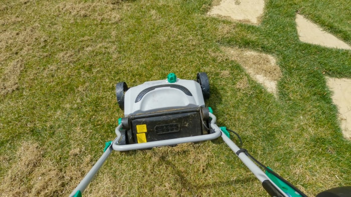 Jardinier utilisant un aérateur de gazon tout en prenant soin de la pelouse de son jardin. Vue à la première personne des travaux de jardinage printaniers pour améliorer la croissance de la pelouse verte. Machines pratiques pour l'aménagement paysager.