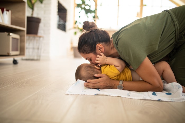 Une mère joue avec son bébé sur le sol stratifié de couleur bois clair.