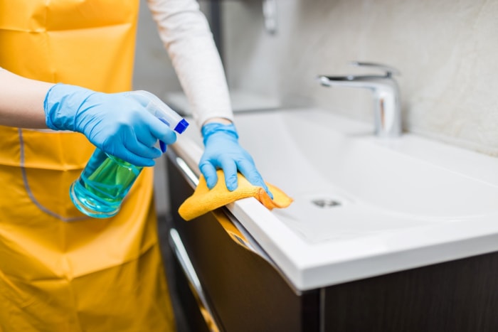 Une personne avec des gants pulvérise de l'eau sur le lavabo de la salle de bain.