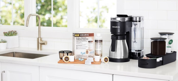 Un kit d'entretien de 3 mois pour cafetière Keurig K-Duo est posé sans emballage sur un comptoir de cuisine blanc à côté d'une cafetière Keurig en acier inoxydable et noire.