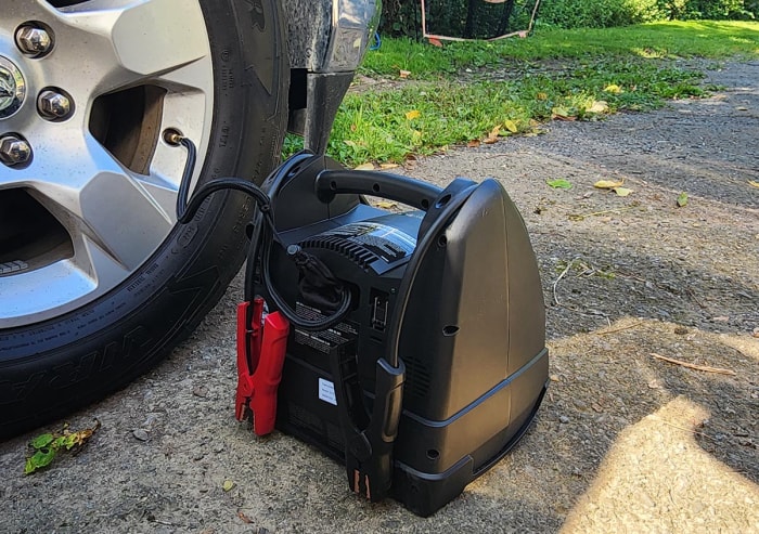 La centrale électrique portable et le démarreur Schumacher sont posés sur le sol à côté d'un pneu de voiture en cours de gonflage.