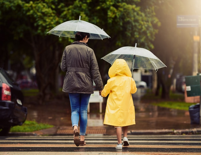 mère et fille en imperméable jaune traversant la rue, tenant toutes deux des parapluies transparents