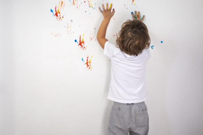 Un petit garçon joue avec de la peinture au doigt en laissant des traces sur un mur blanc.