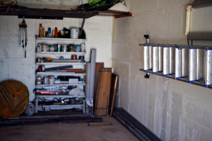 garage intérieur avec murs en briques blanches avec échelle montée sur le mur et une étagère à l'arrière avec des pots de peinture en stockage