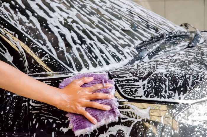 Une personne qui lave une voiture à la main avec un chiffon en microfibres