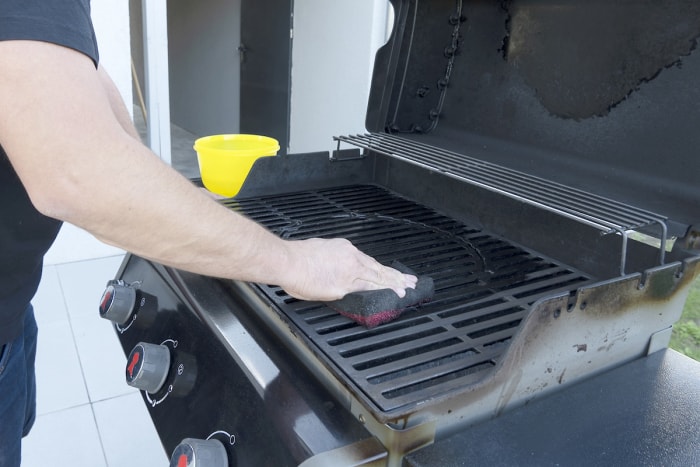 Homme utilisant une éponge pour nettoyer la table de cuisson d'un grill.