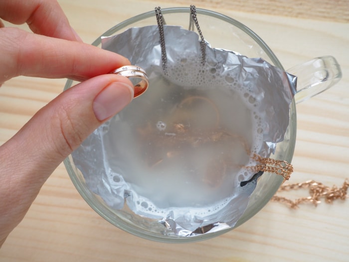 La main laisse tomber la bague en or dans une tasse de solution de nettoyage avec d'autres colliers.