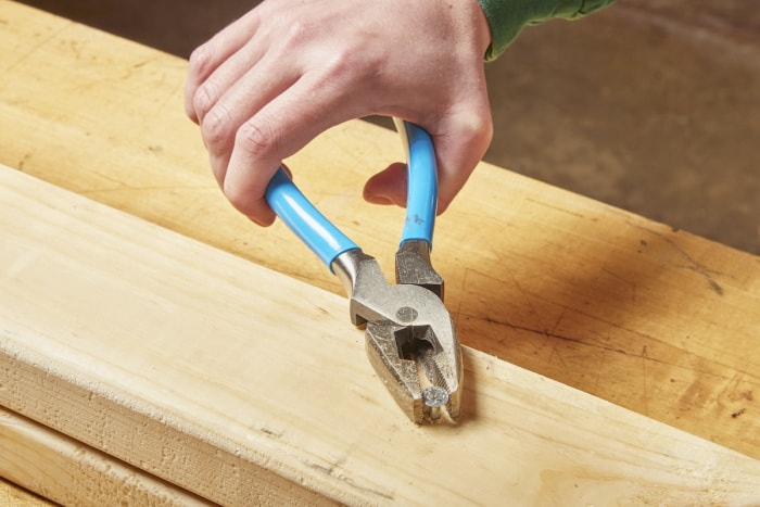 Une personne utilise une pince pour retirer une vis dénudée coincée dans un montant en bois dans un atelier domestique.