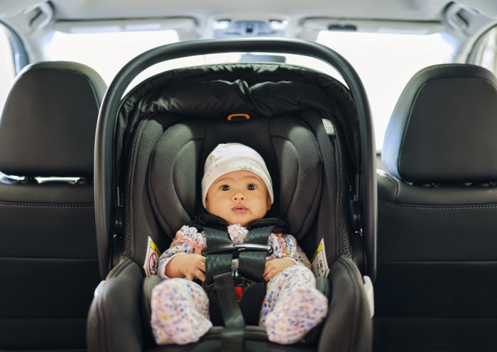 Un bébé de 3 mois assis dans un siège auto sur la banquette arrière d'une voiture.