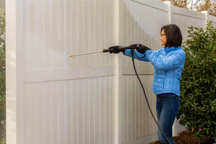 Une personne nettoie sous pression une clôture blanche en utilisant le concentré Ecolab Exterior House & Siding de The Home Depot.