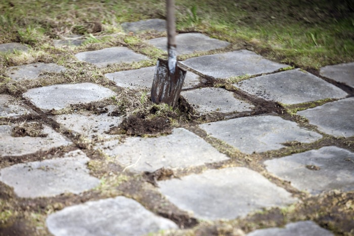 pelle déterrant de vieux pavés d'aménagement paysager en béton pour les recycler ou les donner