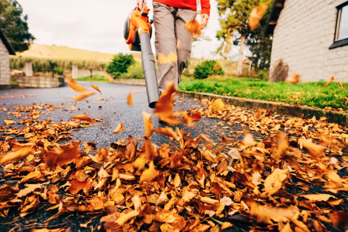 marcher avec un souffleur de feuilles orange soufflant des feuilles brunes dans la rue en automne