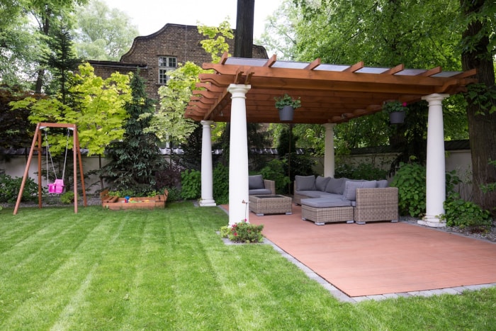 Un jardin clôturé avec un espace de vie extérieur pavé et des meubles de jardin, couvert par une pergola.