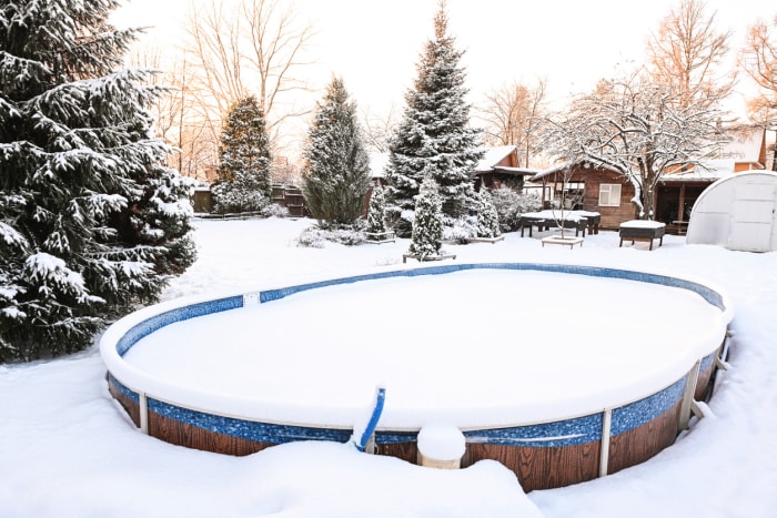 La neige s'est accumulée sur la couverture d'une piscine hors sol dans une propriété résidentielle, parmi des arbres verts enneigés.