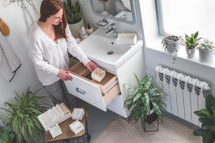 Une jeune femme heureuse se tient devant les tiroirs ouverts de la coiffeuse et sort ses articles de toilette du tiroir. Concept d'économie d'espace et d'organisation de la coiffeuse. Plantes d'intérieur.