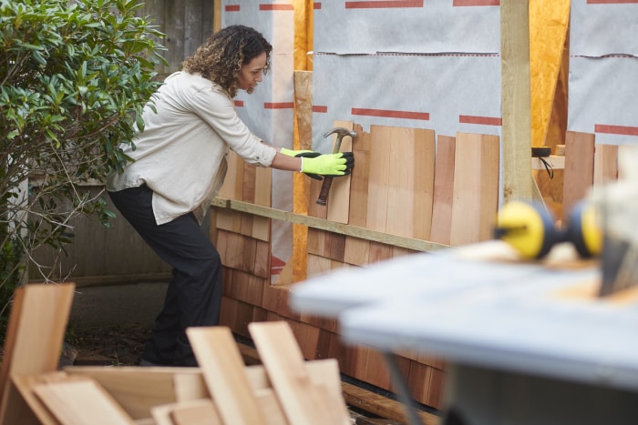 une-femme-travaille-sur-un-abri-en-bois-tout-en-tenant-un-marteau-et-portant-des-gants