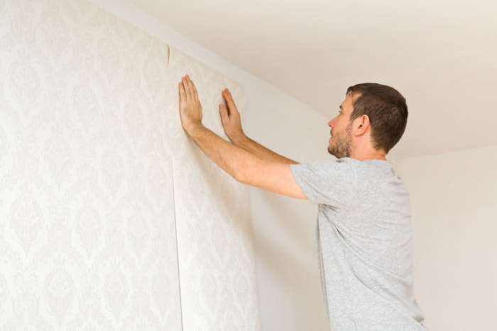 Un jeune homme adulte pose un nouveau papier peint sur un mur blanc. Gros plan. Travaux de réparation à domicile. Vue de côté.