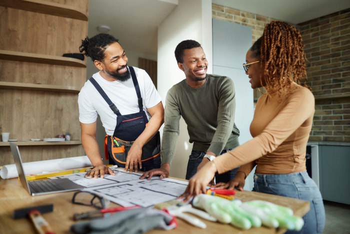 Deux hommes et une femme sourient en examinant des plans de construction. 