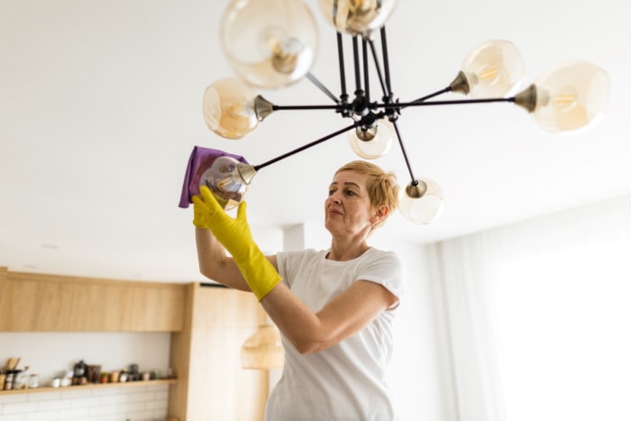 Femme utilisant un chiffon pour nettoyer un luminaire.