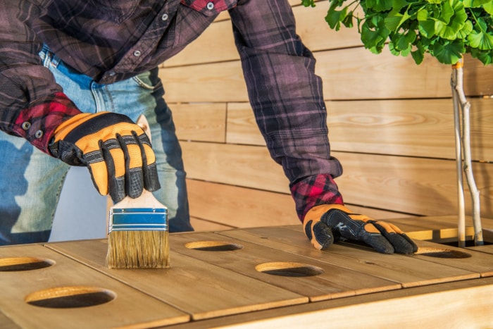 Quelqu'un teint une table en bois à l'extérieur avec un pinceau