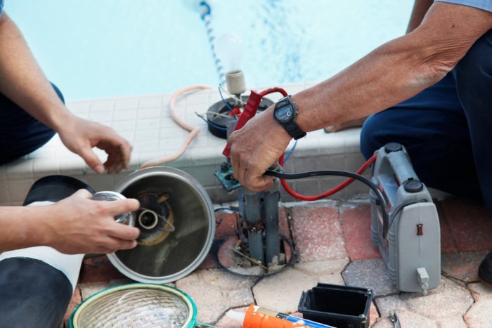 Deux ouvriers utilisent des outils pour réparer une piscine.