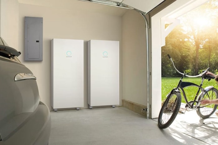 Deux batteries solaires montées sur le mur d'un garage dont la porte est ouverte pour permettre l'entrée et la sortie d'un vélo et d'une voiture.